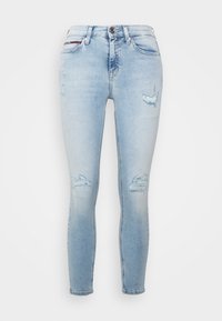 Jeans ajustados de color azul claro con parches desgastados en los muslos y las rodillas, estilo de cinco bolsillos y cierre de botón en la cintura.