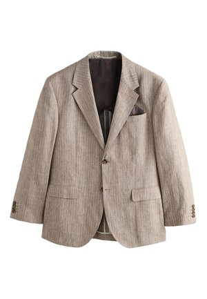 Ung mand iført en beige pinstripe jakkesæt og en blå skjorte, stående nær stentrin foran en hvid struktureret væg.