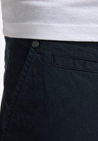 Marine shorts med en struktureret overflade, der har en frontknaplukning og en baglomme. Materialet ser ud til at være slidstærkt og let.