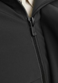 Čierna bunda s hladkou textúrou, predĺženým strihom a výraznými detailmi zipsu. Zips je matne čierny s logom na ťaháku.