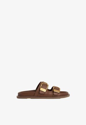 Brown leather slide sandals featuring two large gold-tone buckles, a flat sole, and white stitching along the edge.