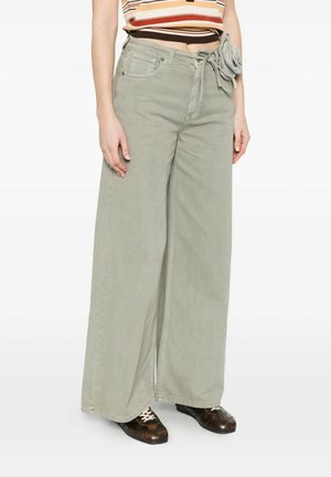 Persona che indossa pantaloni larghi grigio chiaro a vita alta con cintura annodata e scarpe stringate marroni decorate, top corto a righe visibile.