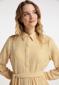 Geel bloemen blousejurk met lange mouwen, geplooide taille en een zachte, textuurstof met een klein, verspreid patroon.