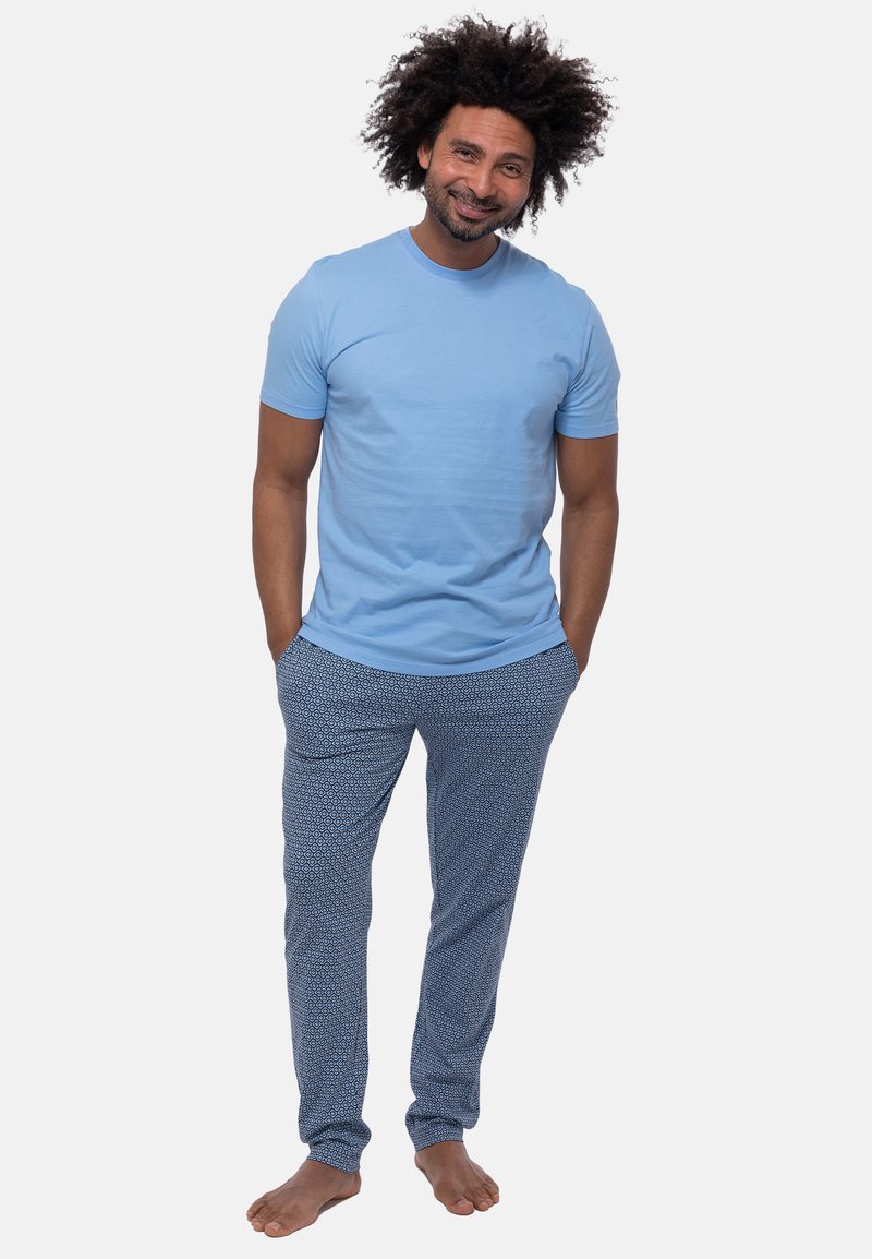 Hellblaues Baumwoll-T-Shirt mit Rundkragen, kombiniert mit blauen Pyjamahosen mit weißen geometrischen Mustern. Lässige Passform, barfuß.