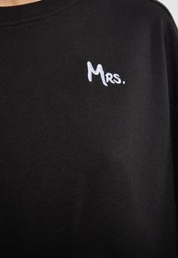 Felpa nera in cotone con testo ricamato bianco "Mrs." sul lato sinistro. Il tessuto è liscio e presenta un design con collo a girocollo.
