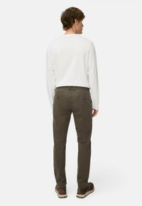 Dunkelgrüne Baumwollhose mit zwei hinteren Taschen, kombiniert mit einem weißen Langarmhemd. Die Passform ist leger mit einem geraden Beindesign.