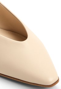 Vaaleanbeige nahkakenkä, jossa on terävä kärki ja leikkaus yksityiskohta sivussa. Sujuva pinta, minimalistinen muotoilu ja ohut pohja.