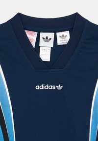 Αθλητική φανέλα σε σκούρο μπλε χρώμα με λαιμόκοψη σε σχήμα V, με λευκές και ανοιχτό μπλε ρίγες, υφή υφάσματος και το λογότυπο της Adidas σε λευκό. Ορατές ετικέτες φροντίδας.