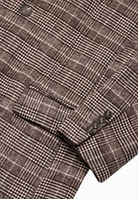 Villatakki harmaissa sävyissä, jossa on tekstuuri, notched-kaulus ja neljä mustaa nappia hihoissa.