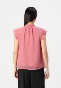 Blusa rosa a pois con maniche corte arricciate, collo alto e vestibilità ampia. Tessuto trasparente con una texture liscia, dettaglio di design a strati sul retro.