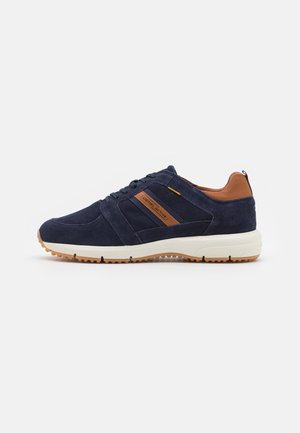 Navy suede sneaker with tan accents, white midsole, and textured rubber sole. Features lace-up design and branding on the side.