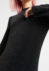 Pull noir à manches longues avec une coupe ajustée, doté d'une surface texturée ornée de paillettes argentées et d'un col rond.