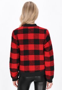 Maglione a scacchi rosso e nero con maniche lunghe, colletto e polsini a coste, realizzato in un tessuto a maglia testurizzato.