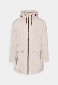 Ljusbeige vattentålig jacka med dragkedja fram, justerbar huva, två framfickor och svarta detaljer på dragkedjan och snoddarna.