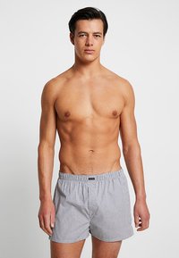 Boxershorts in blauen und weißen vertikalen Streifen, mit einem elastischen Bund und einem kleinen Logostick auf der Vorderseite. Glatte Stofftextur.