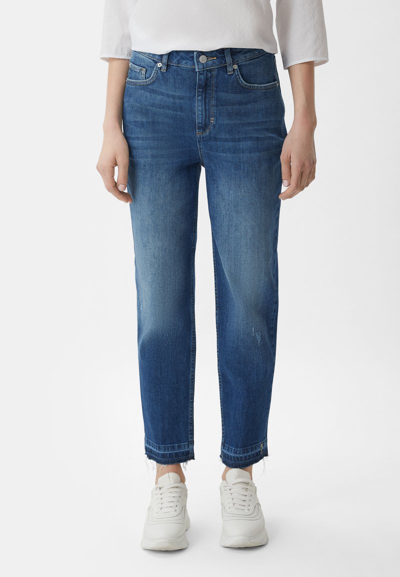 Jasnoniebieskie dżinsy o prostym kroju, z średnim stanem, postrzępionymi brzegami i delikatnym wyblaknięciem, w połączeniu z białymi sneakersami.