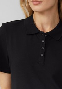 Polo noir avec un col classique, des manches courtes et une patte de boutonnage à cinq boutons. Le tissu a une finition texturée.