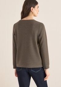 Brown, long-sleeve top with a textured, small dot pattern; features a crew neck and a relaxed fit, paired with dark blue jeans.