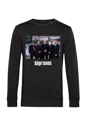 Cinque uomini in abiti scuri in piedi in un cimitero con il testo "I Soprano" sotto su una maglietta a maniche lunghe nera.