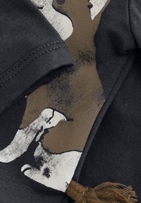 Svart bomullströja med en grafik som har en brun djurdesign på framsidan. Inkluderar en texturerad tyg och ett brunt tofsakcent.