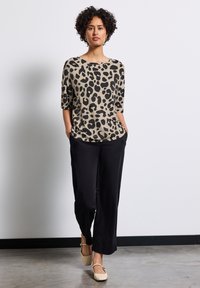 Beige leopard-print top with wide neckline and three-quarter sleeves, paired with black wide-leg trousers and neutral flats.