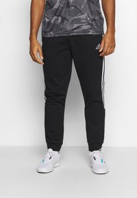 Zwarte trainingsbroek met witte zijsstripes, met een tapered leg ontwerp. De stof is glad en zacht, geschikt voor casual kleding.
