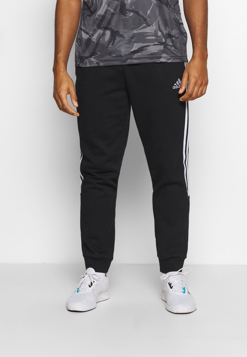Zwarte trainingsbroek met witte zijsstripes, met een tapered leg ontwerp. De stof is glad en zacht, geschikt voor casual kleding.