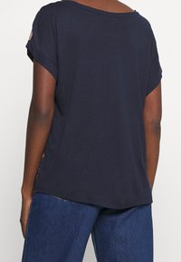 Granatowa, krótko rękawowa koszulka z szerokim dekoltem i podwiniętymi mankietami, wykonana z miękkiego materiału, z luźnym krojem i subtelnymi detalami ściegów.