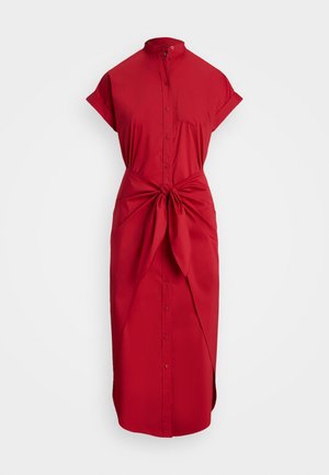 Rdeča obleka s kratkimi rokavi, ovratnikom, sprednjim žepom in pripetim detajlom v pasu. Gladek material in dolžina do sredine tele.