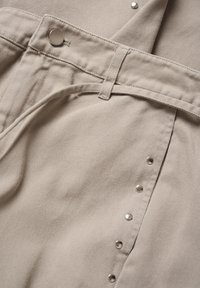 Beige strukturväv med ribbat mönster, utrustad med bältesöglor, knappar med tryckknapp och en vikt design. Hållbart material med en slät finish.