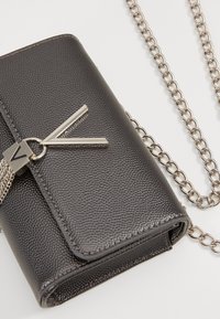Pelēka teksturēta mākslīgā āda crossbody soma ar sudraba ķēdes siksnu un sudraba metāla aksesuāru ģeometriskā formā.