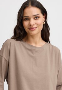 Lysbrun oversized t-shirt lavet af blødt bomuldsstof, med rund hals og sænkede skuldersømme, der skaber en afslappet pasform.