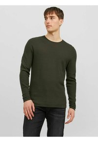 Langærmet, mørkegrøn skjorte i struktureret strikmateriale med rund halsudskæring og tætsiddende ærmer, båret med mørke jeans.