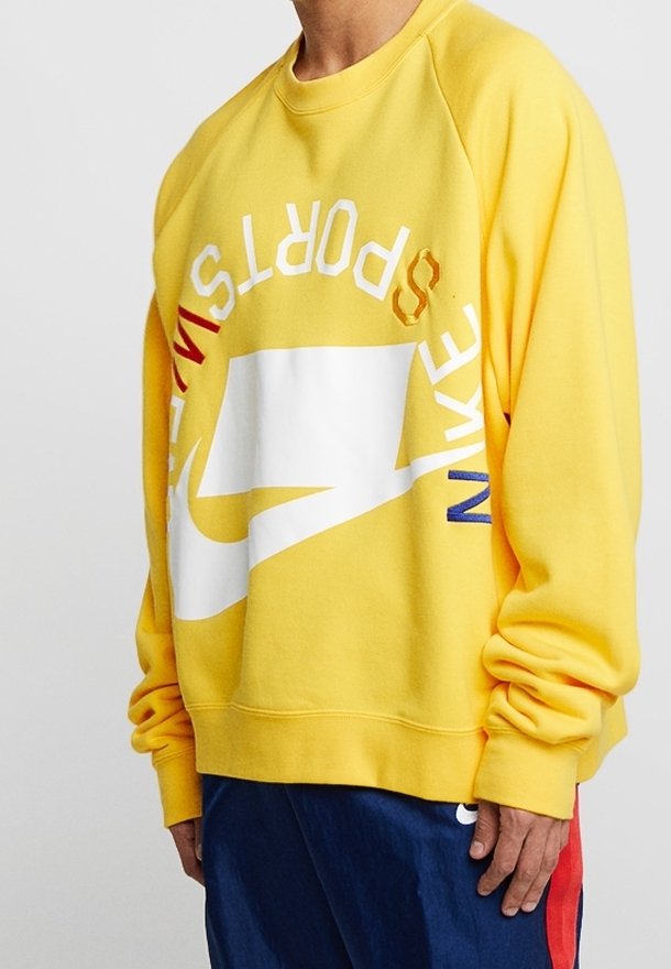 Felpa gialla con vestibilità oversize, caratterizzata da un logo Nike bianco e testo multicolore. Realizzata in materiale morbido con polsini a coste.