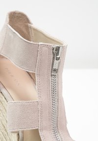 Sandalo con zeppa in suede rosa chiaro, dotato di cerniera laterale e cinturino elasticizzato. Suola texturizzata e rivestimento interno liscio.