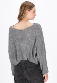 Grau gestrickter Pullover mit weitem Bootsausschnitt, lockerer Passform und geripptem Saum. Die Textur ist weich, und die Ärmel sind lang und lässig.