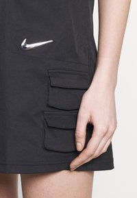 Czarna odzież z trzema bocznymi kieszeniami, z metalicznym, srebrnym logo Nike. Materiał wydaje się gładki i lekki.