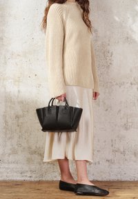 Maglione a maglia beige, gonna color crema e borsa a spalla in pelle nera con doppi manici. Le ballerine nere completano l'outfit. Design semplice e minimal.