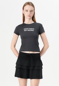 Black cropped t-shirt with white text "CATCH FLIGHTS NOT FEELINGS." Paired with a black layered ruffle skirt featuring a drawstring waist.