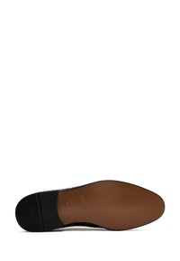 Semelle de chaussure en cuir noir avec un motif texturé, présentant un dessous lisse brun et un petit accent noir au niveau du bout.