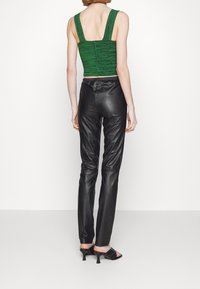 Zelený textured krácený top s širokými ramínky a zipovým zap ínáním, kombinovaný s úzkými černými koženými kalhotami a sandály na holé noze s vysokým podpatkem.