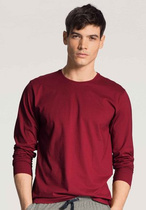 Bordeaux langarm t-shirt van een zachte, gladde stof met een ronde halslijn. Gecombineerd met lichtgrijze joggingbroek met koord, wat een casual stijl toont.