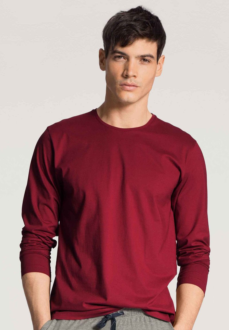 Bordeaux langarm t-shirt van een zachte, gladde stof met een ronde halslijn. Gecombineerd met lichtgrijze joggingbroek met koord, wat een casual stijl toont.