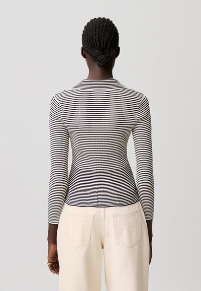 Top de manga larga de rayas blancas y negras con un diseño ceñido, escote redondo y textura suave. Combinado con pantalones color crema.