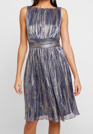 Sleeveless silver and blue metallic dress with boat neckline, fitted waistband, and pleated A-line skirt, worn by a person with dangling earrings.