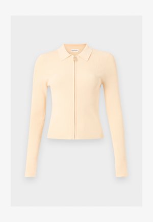 Top beige de punto acanalado de manga larga con cuello y cremallera frontal, ajuste ceñido, mostrado sobre un fondo gris claro liso.