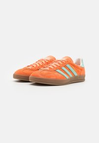 Orange suede sneakers with turquoise stripes, a brown rubber sole, and white lining. Features a textured tongue and lace-up design.