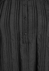 Crna košulja s gumbima napravljena od teksturirane, naborane tkanine, koja ima vertikalne pruge i šest malih crnih gumba duž prednje strane.