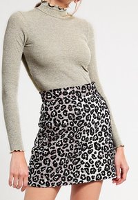 Pull à col roulé à manches longues en rib doux de couleur vert olive métallique, associé à une mini-jupe ajustée en imprimé léopard avec un schéma de couleurs noir et crème.