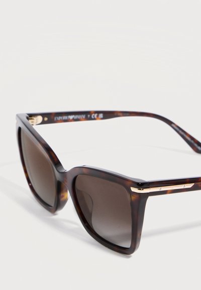 Γυαλιά ηλίου με τετράγωνο σκελετό σε σχέδιο χελώνας, σκούρους φακούς με βαθμιαία απόχρωση και λεπτές χρυσές διακοσμήσεις στους βραχίονες.